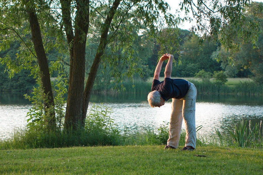Mann macht Gymnastik auf einer Wiese am Teich