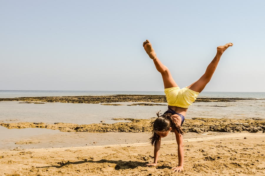 Ein Mädchen macht einen Handstand an einem Sandstrand